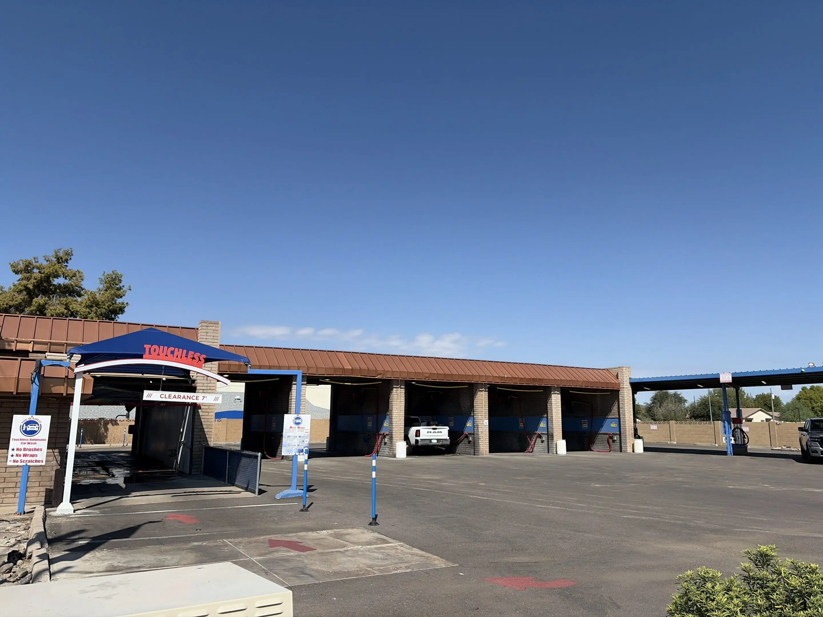 Gas station with a car parked in front of it, surrounded by plants, trees, and a shed