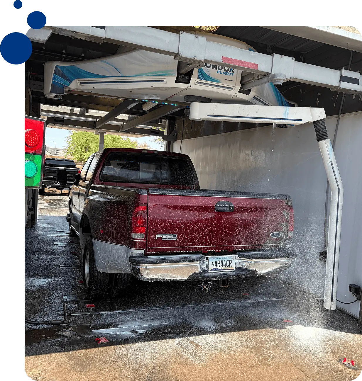 Red truck parked in a garage with a hose attached to it, surrounded by trees and a clear blue sky